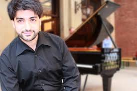 A man posing for a picture with a piano behind her
