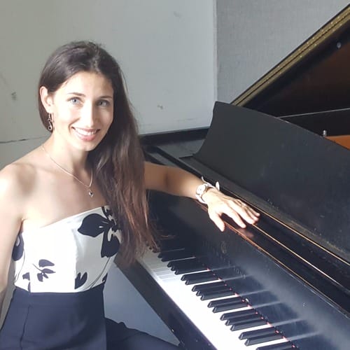 A woman posing for a picture beside a piano