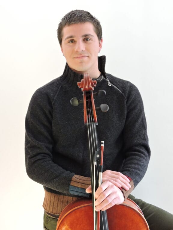 A young man posing for a picture with his cello
