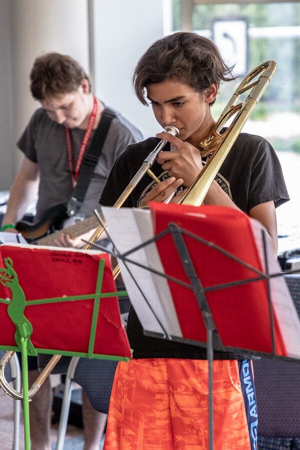 boy playing trombone with guitar player in the background