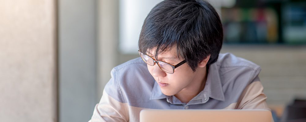 Young Asian man writing on notebook and working with laptop computer in college building