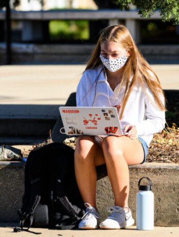 Young student working on laptop with UW W logo on campus mall