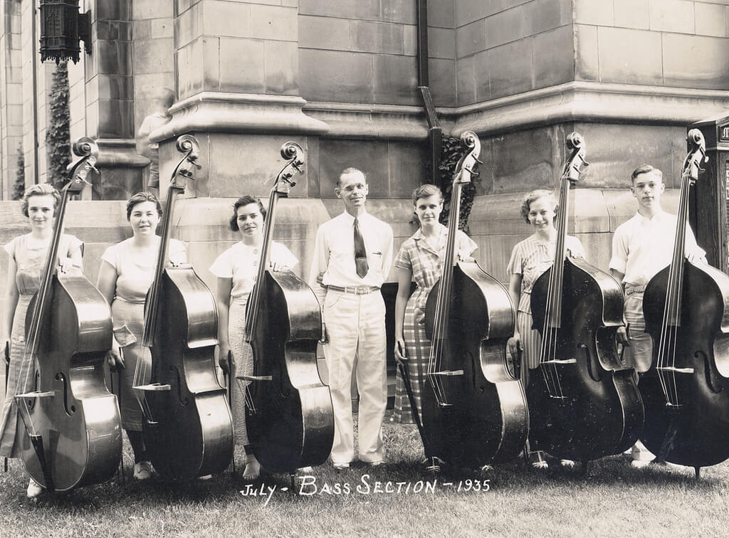 six bass students standing with their instruments and teacher in front of university building