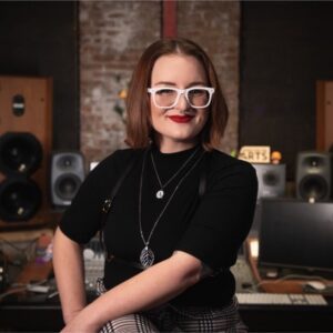 Audrey Martinovich sits surrounded by music production equipment in a studio